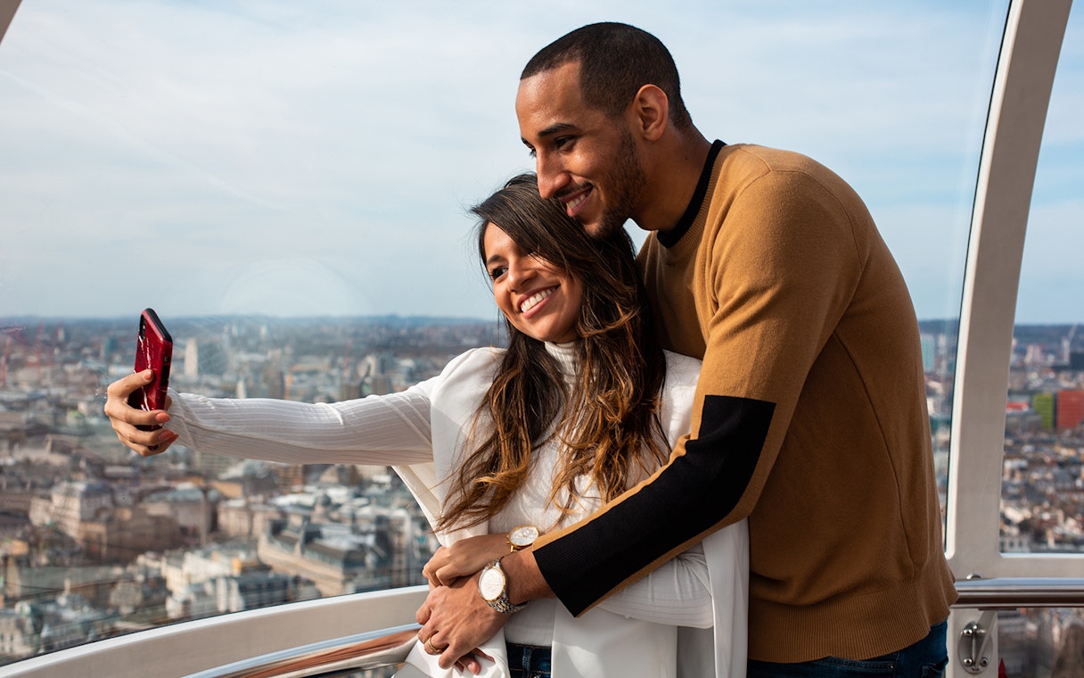 Couple taking a selfie on the London Eye with cityscape view.