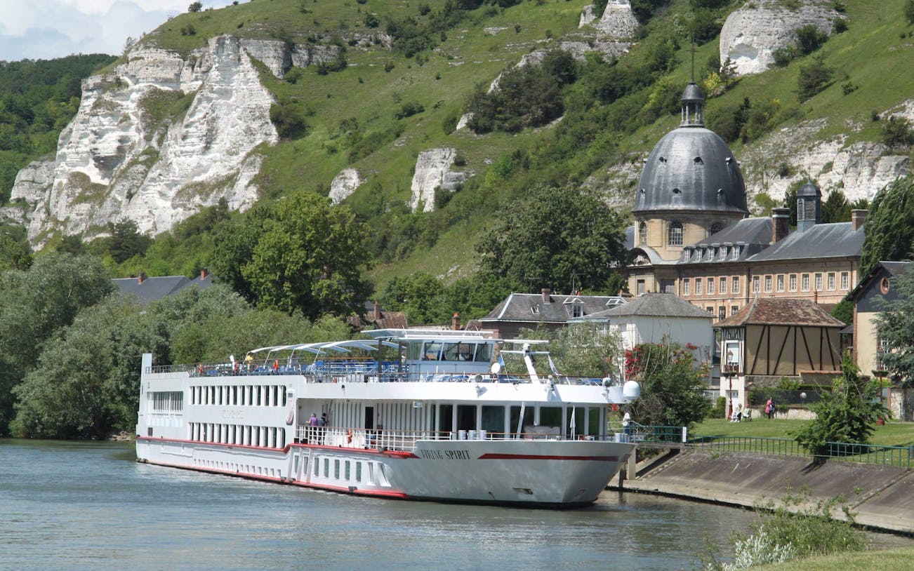 Seine River cruise ship docked near historic buildings and cliffs.