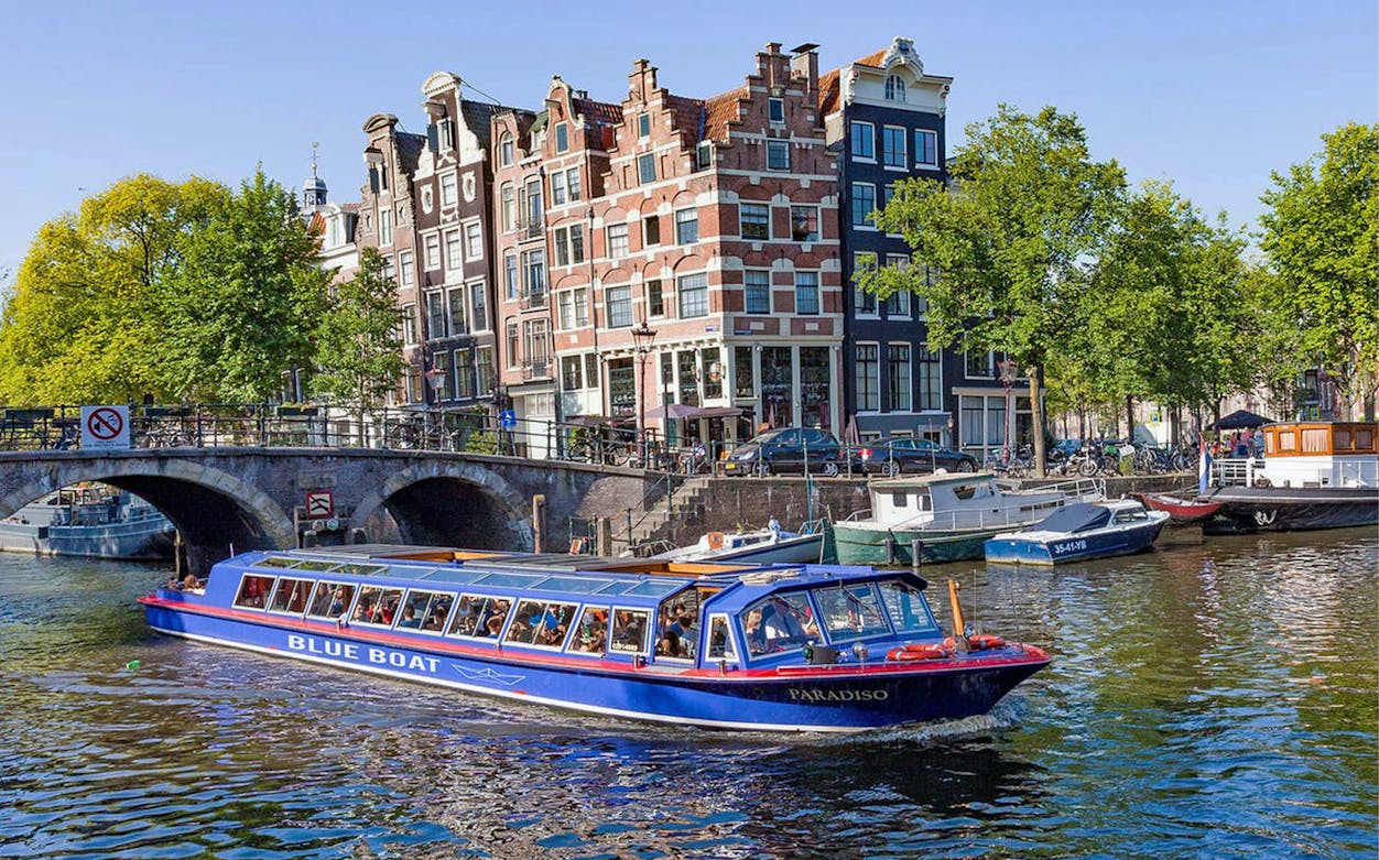 Canal cruise boat on Amsterdam canal with historic buildings and bridge in view.