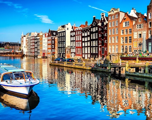 Canal cruise boats on Amsterdam canal with historic buildings in the background.