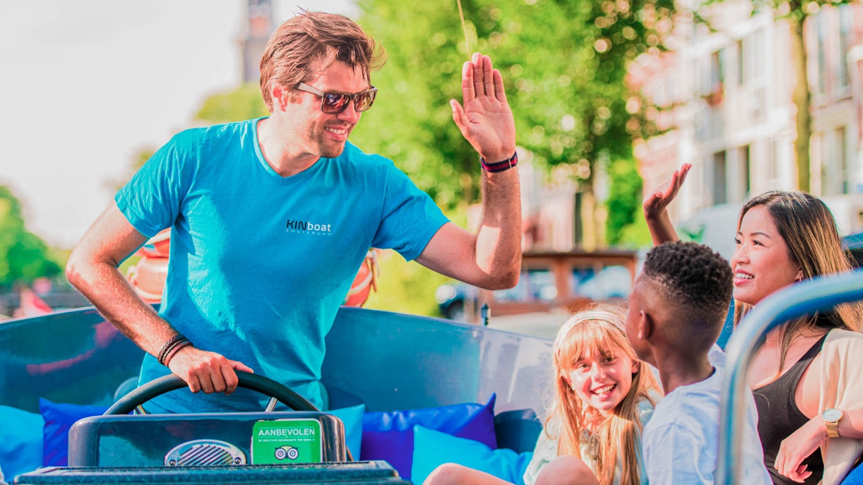 Man steering small boat on canal cruise with smiling passengers in Amsterdam.