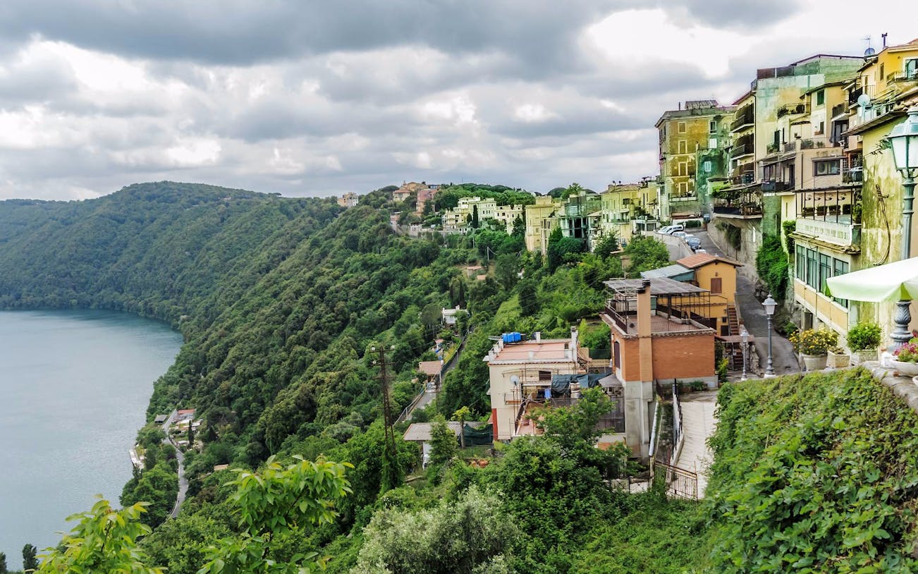 Hillside view of Castelli Romani with lush greenery and buildings overlooking a lake.