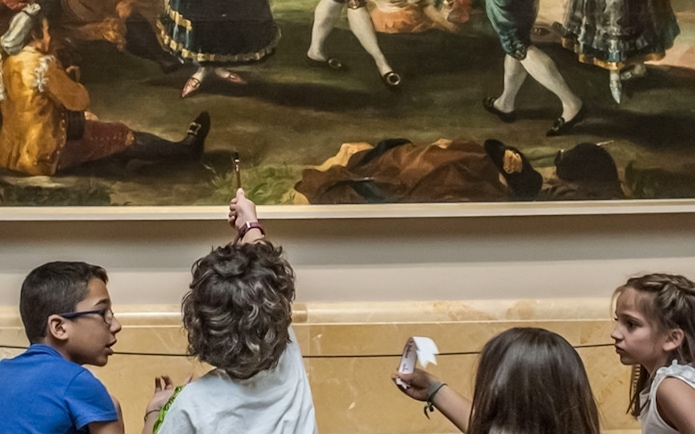 Children observing a painting at Prado Museum with audio guides.
