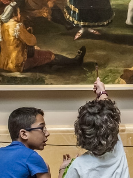 Children observing a painting at Prado Museum with audio guides.
