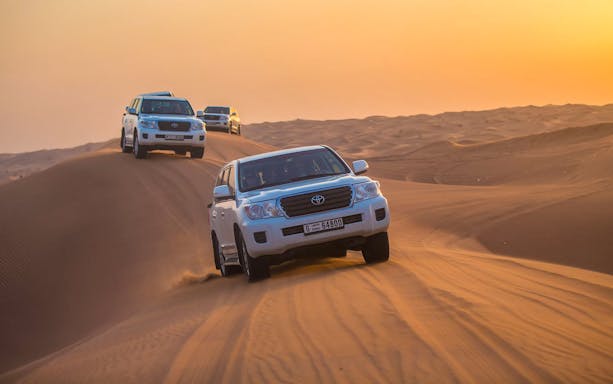 Desert safari with SUVs driving over sand dunes at sunset in Dubai.