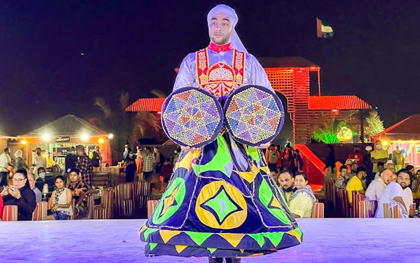 Performer in traditional attire during a desert safari show with audience in Dubai.
