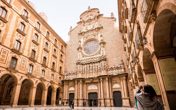 Montserrat monastery facade with tourists exploring the courtyard.