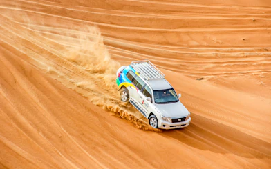 SUV driving through desert dunes during sunrise safari.