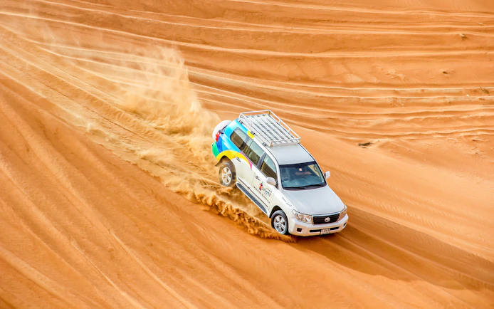 SUV driving through desert dunes during sunrise safari.