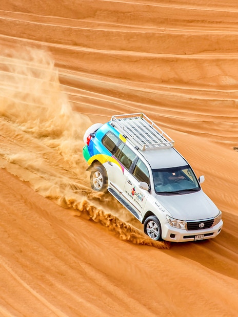 SUV driving through desert dunes during sunrise safari.