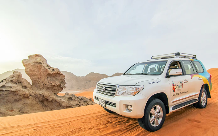 SUV on desert dunes during sunrise, part of a Sunrise Desert Safari with Picnic Breakfast.