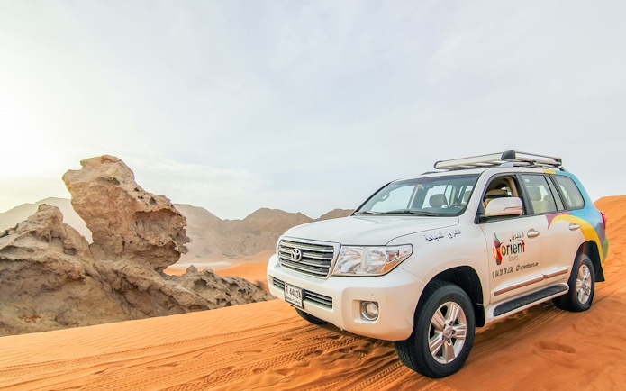 SUV on desert dunes during sunrise, part of a Sunrise Desert Safari with Picnic Breakfast.