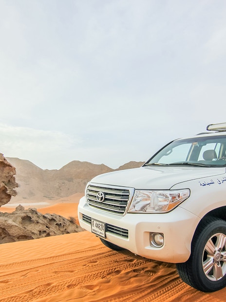 SUV on desert dunes during sunrise, part of a Sunrise Desert Safari with Picnic Breakfast.