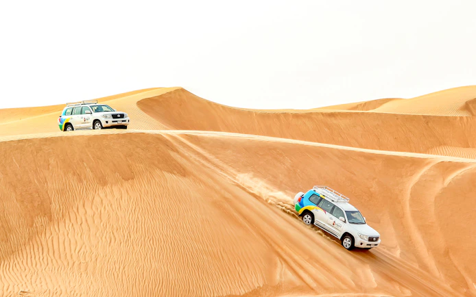 Desert safari vehicles driving over sand dunes during sunrise tour.
