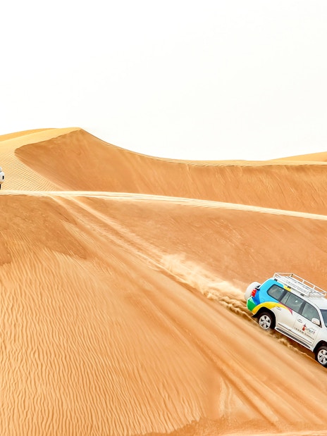 Desert safari vehicles driving over sand dunes during sunrise tour.