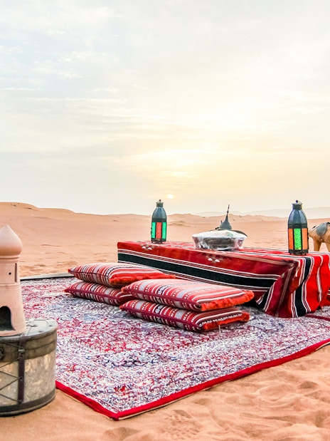 Desert picnic setup with cushions and lanterns at sunrise during a safari.