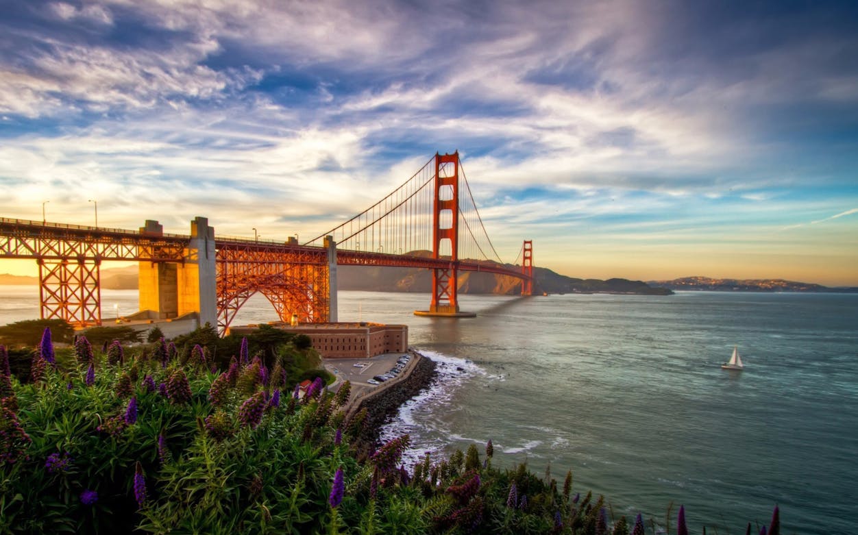 Golden Gate Bridge at sunset with sailboat on San Francisco Bay.