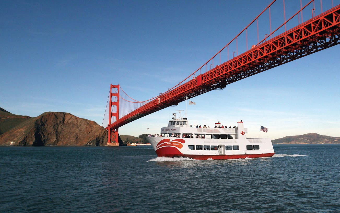 Cruise ship sailing under Golden Gate Bridge during California sunset tour.