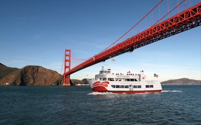 Cruise ship sailing under Golden Gate Bridge during California sunset tour.