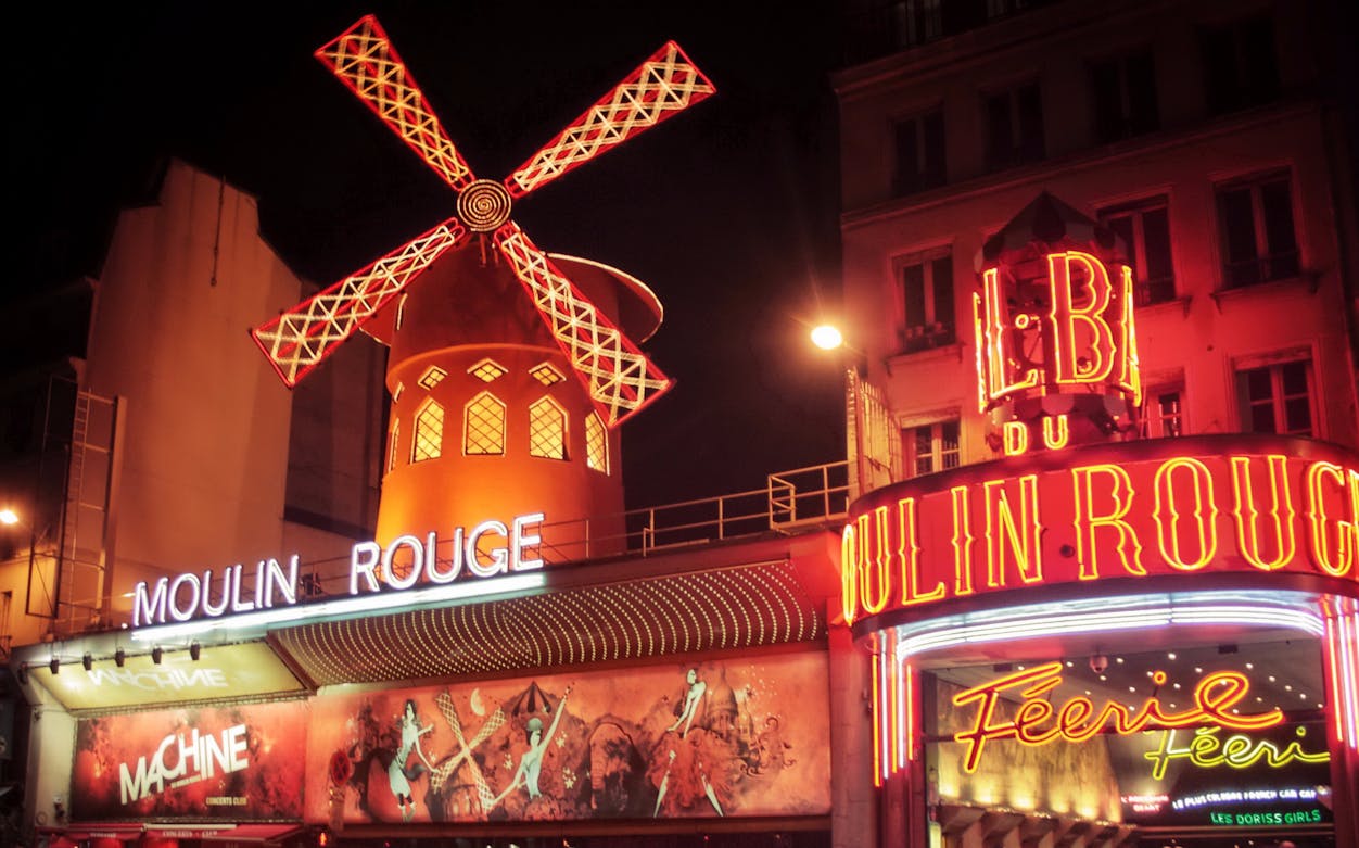 Moulin Rouge entrance with illuminated windmill in Paris at night.