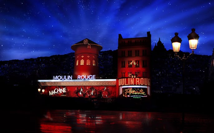 Moulin Rouge illuminated at night in Paris, showcasing vibrant red lights and iconic windmill.