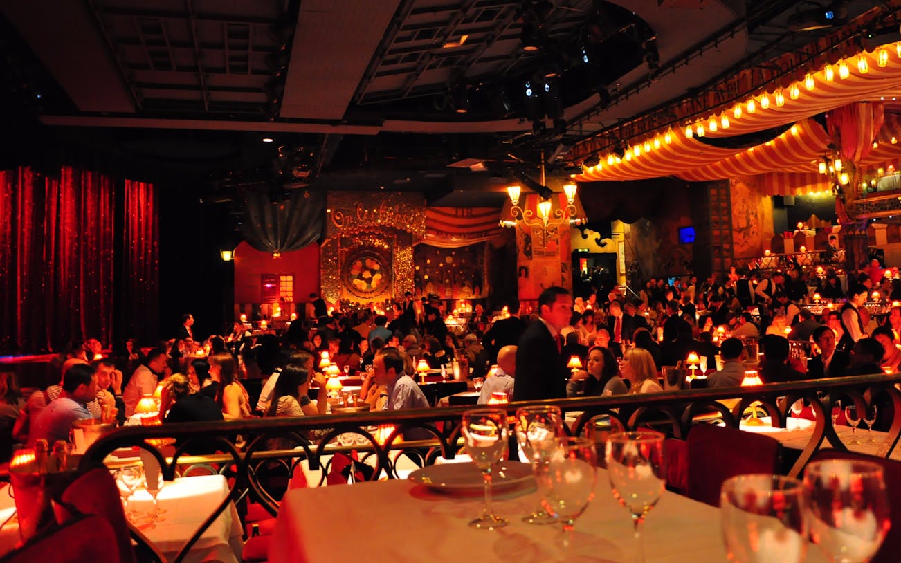 Moulin Rouge dinner show with guests seated at tables in a vibrant Parisian cabaret setting.