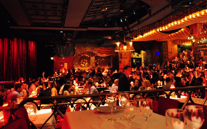Moulin Rouge dinner show with guests seated at tables in a vibrant Parisian cabaret setting.