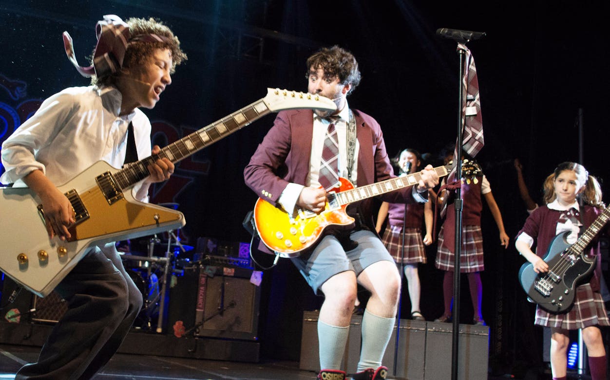 Children performing rock music on stage in school uniforms, School of Rock musical.
