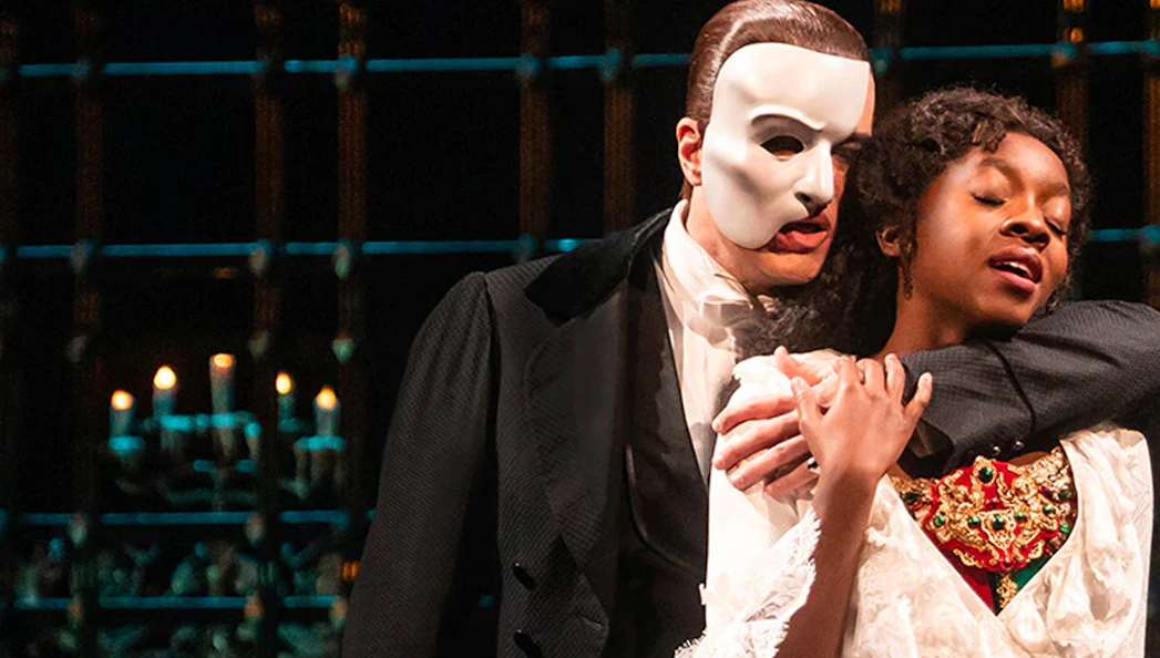 Phantom of the Opera scene with masked character embracing a woman on stage.
