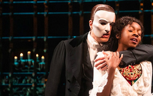 Phantom of the Opera scene with masked character embracing a woman on stage.