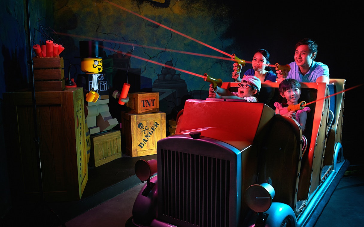 Family enjoying interactive ride at LEGOLAND® Dubai with LEGO characters and laser guns.