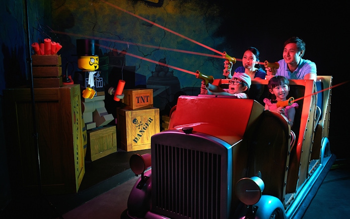 Family enjoying interactive ride at LEGOLAND® Dubai with LEGO characters and laser guns.