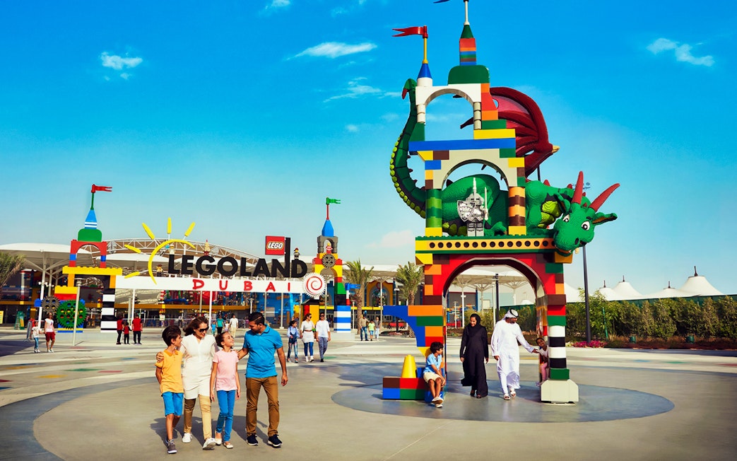 Family walking in front of Legoland Dubai entrance with colorful Lego dragon arch.