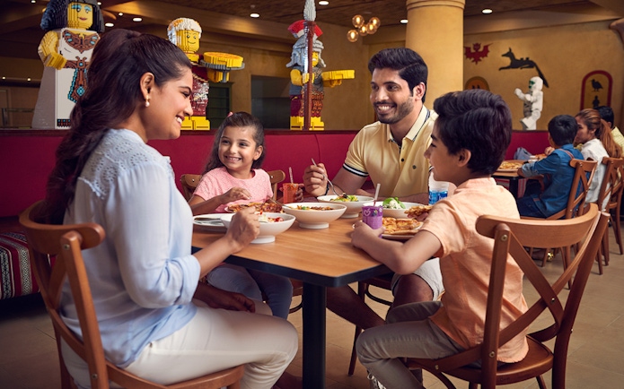 Family dining at LEGOLAND® Dubai restaurant with LEGO figures in the background.