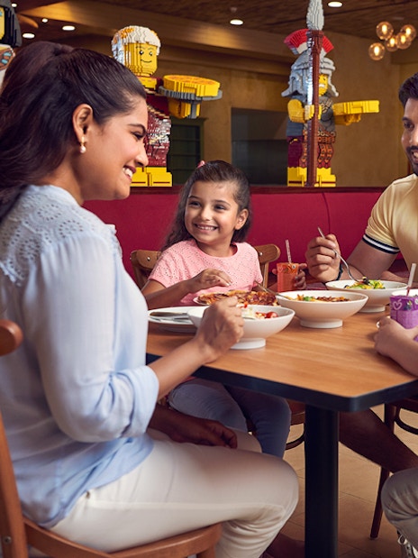 Family dining at LEGOLAND® Dubai restaurant with LEGO figures in the background.