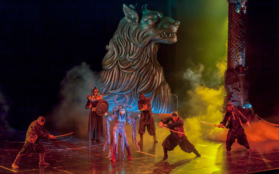 Performers in a theatrical show at Dubai Parks and Resorts with a large wolf sculpture in the background.