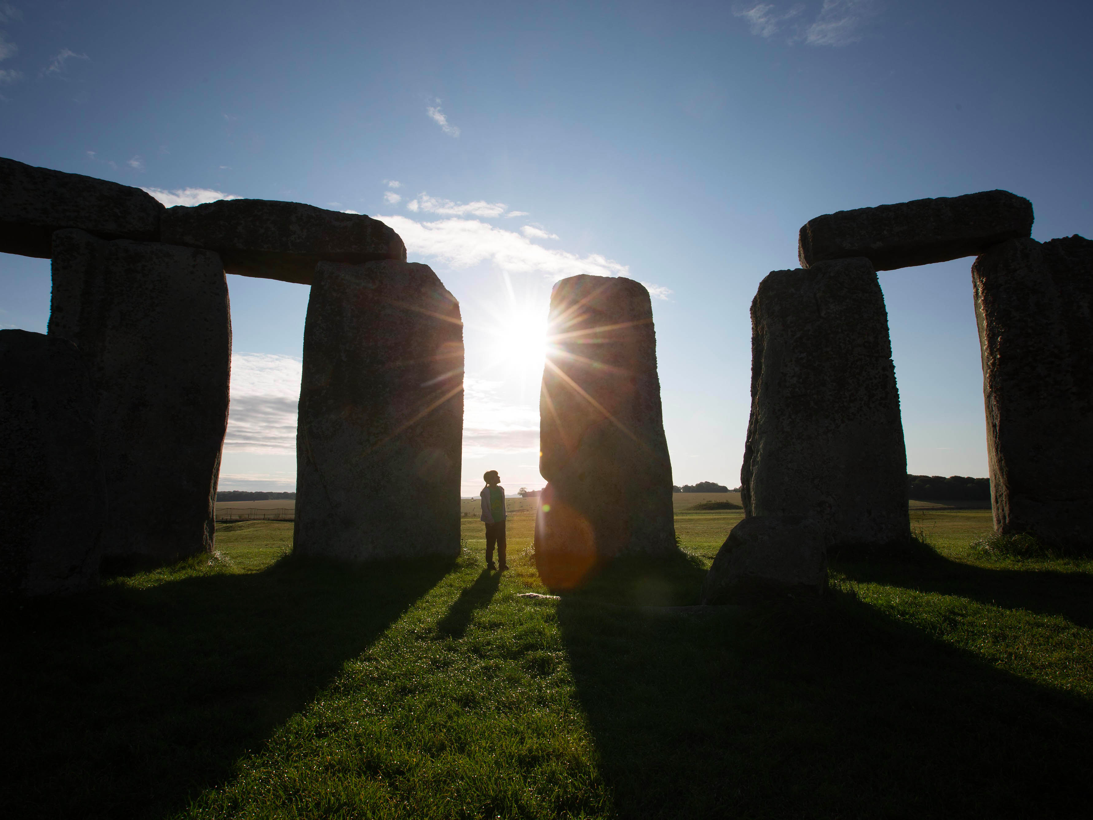 Stonehenge at sunrise with a visitor silhouetted, part of the Stonehenge Express Tour from London.