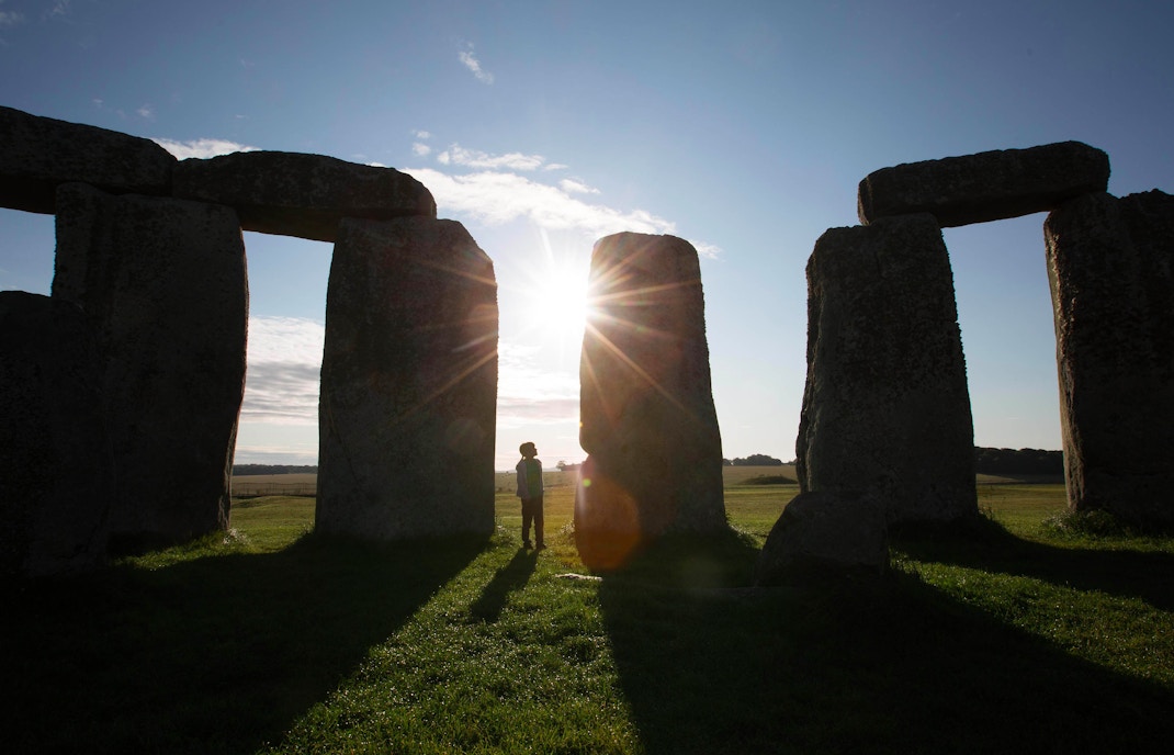 Stonehenge at sunrise with a visitor silhouetted, part of the Stonehenge Express Tour from London.