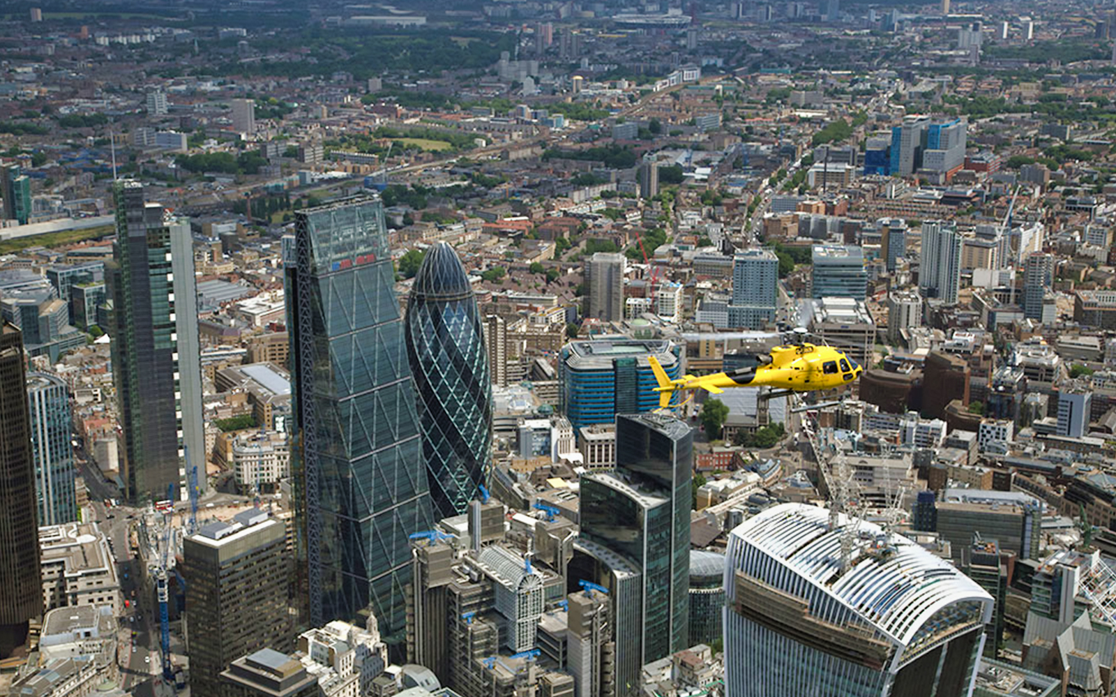 Yellow helicopter flying over London's skyline with the Gherkin building in view.