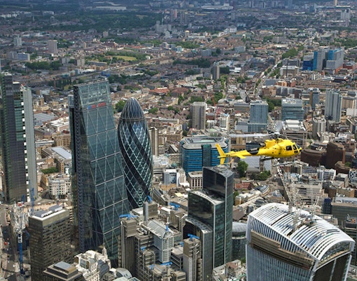 Yellow helicopter flying over London's skyline with the Gherkin building in view.