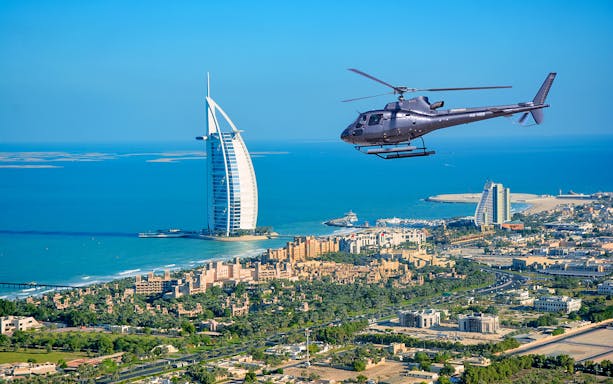 Helicopter flying over Dubai coastline with Burj Al Arab in view.