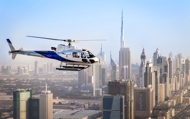 Helicopter flying over Dubai skyline with Burj Khalifa in view.