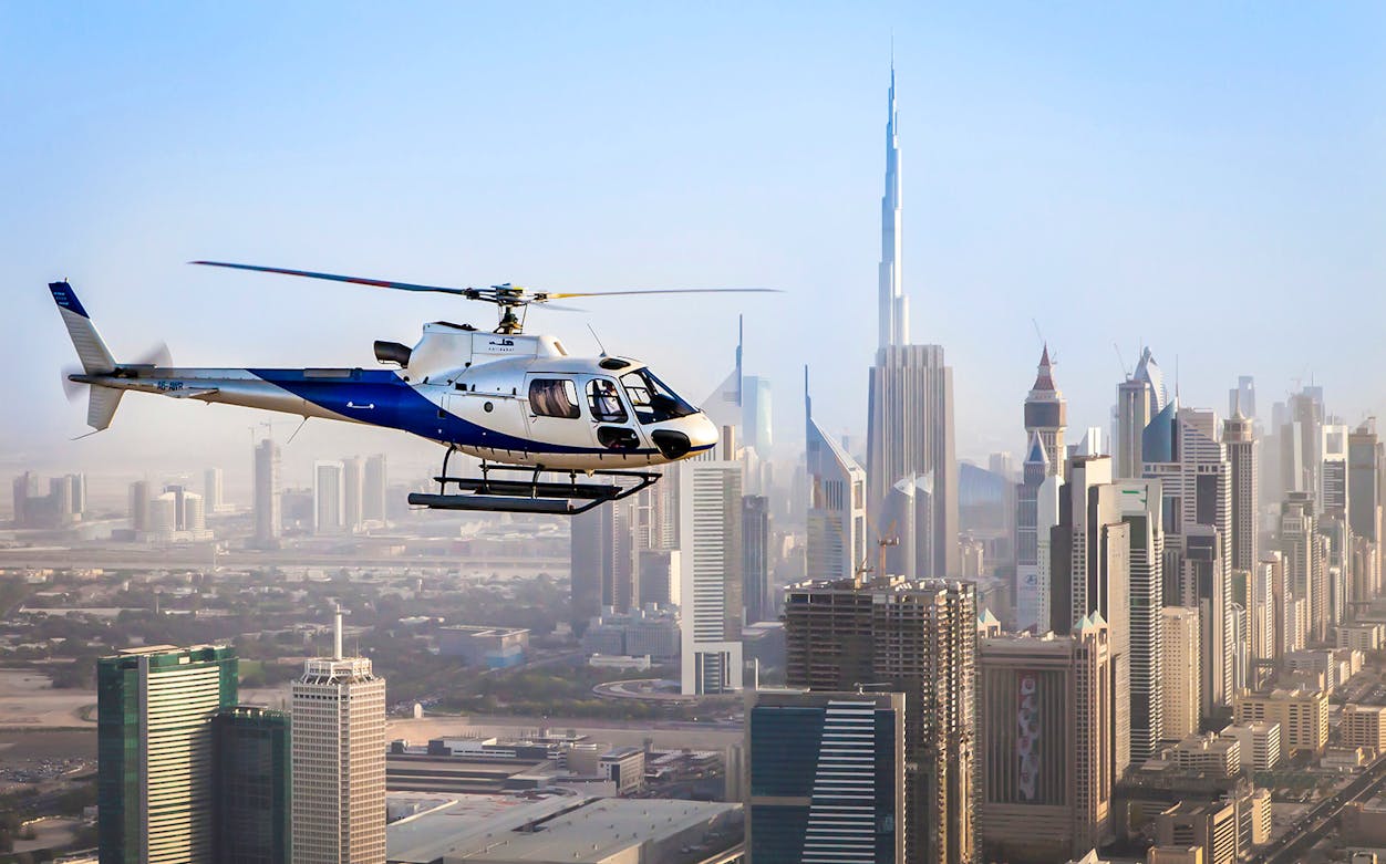 Helicopter flying over Dubai skyline with Burj Khalifa in view.
