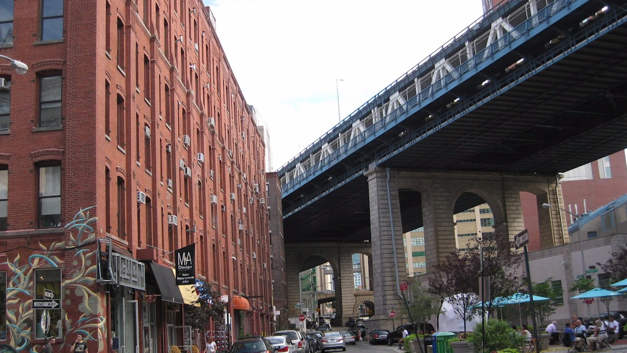 Brooklyn street view with red brick buildings and Manhattan Bridge overhead.