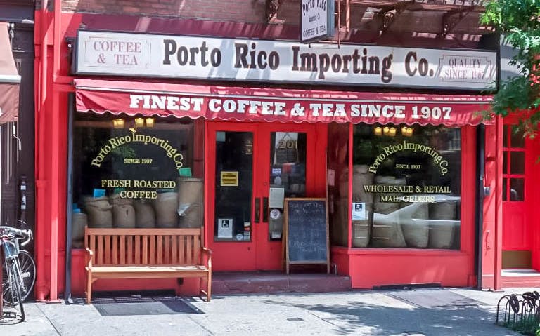 Porto Rico Importing Co. storefront in New York, featuring coffee bags and a bench.