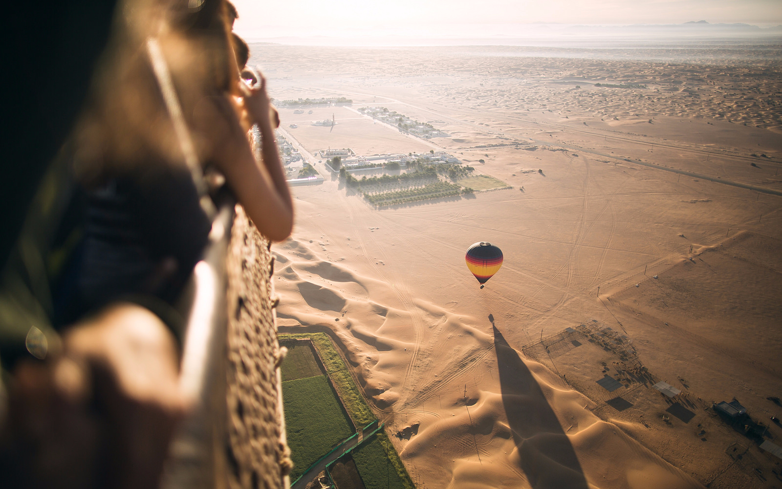 Hot air balloon over Dubai desert landscape with tourists observing from basket.