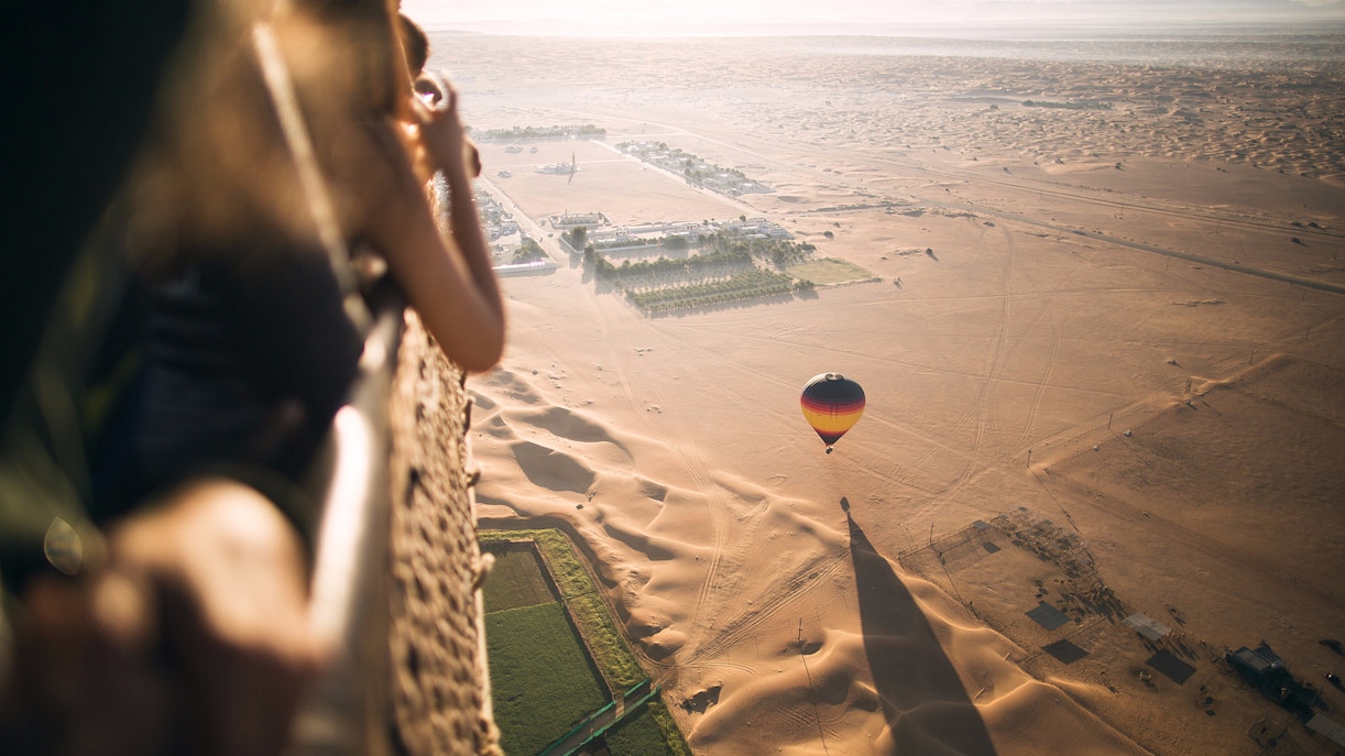 Hot air balloon over Dubai desert landscape with tourists observing from basket.