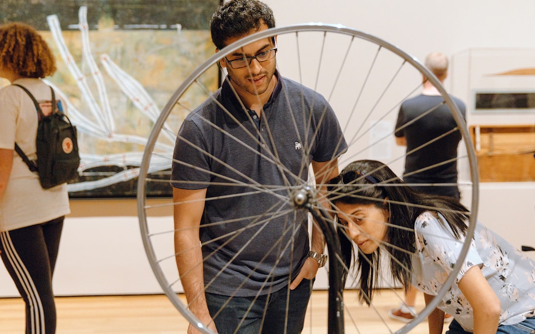 Visitors observing bicycle wheel art at Whitney Museum of American Art.