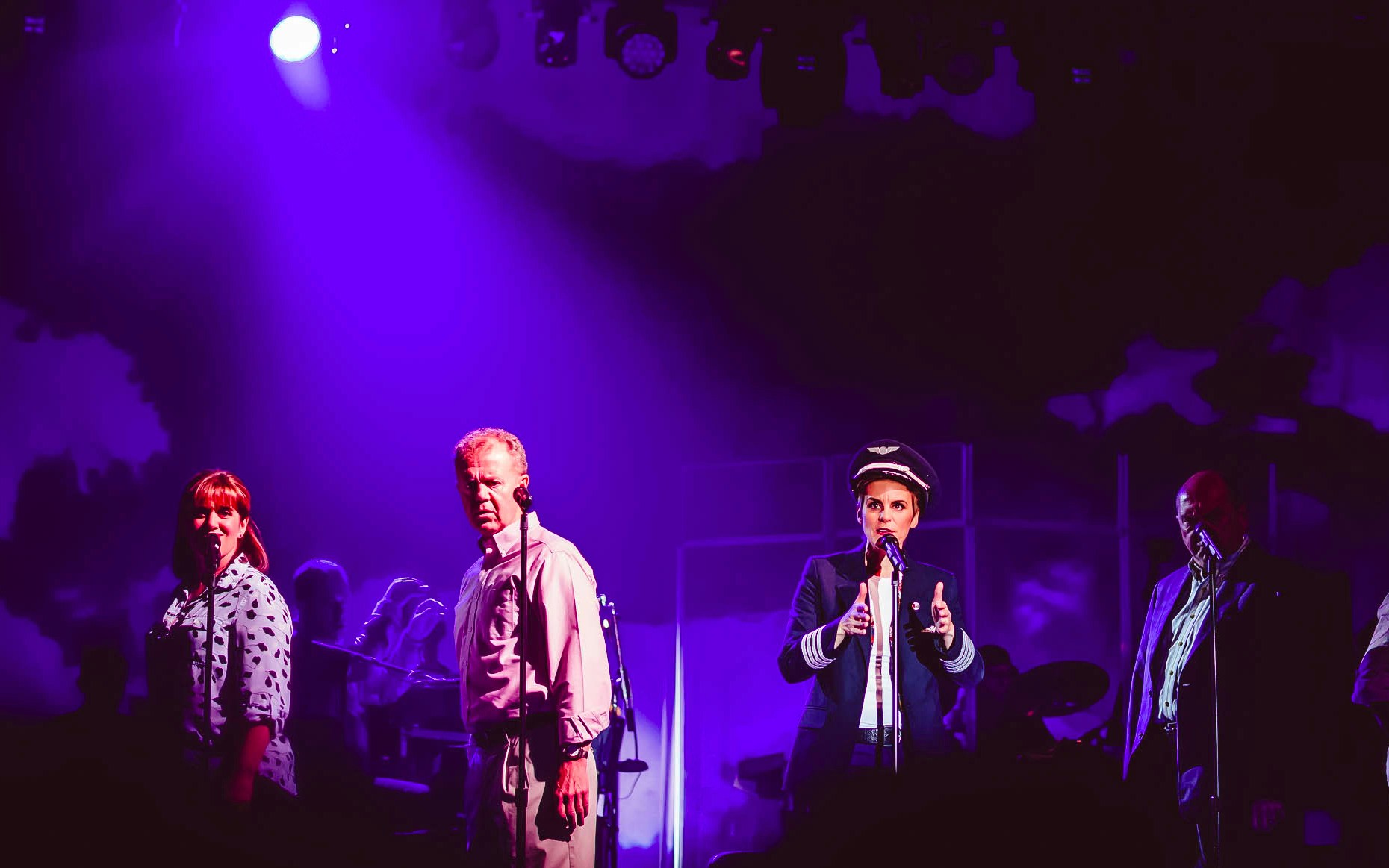 Stage performance of "Come From Away" with actors under purple lighting.