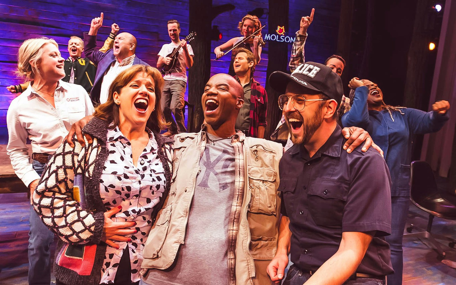 Cast of "Come From Away" performing on stage, expressing joy and camaraderie.